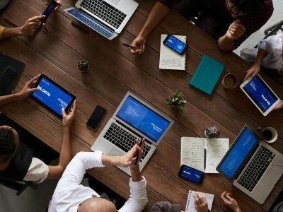 Overhead view of a diverse team discussing around a wooden table, using technology.
