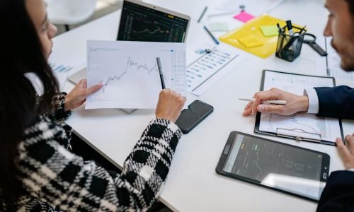 Two colleagues analyzing financial graphs during a business meeting in a modern office setting.